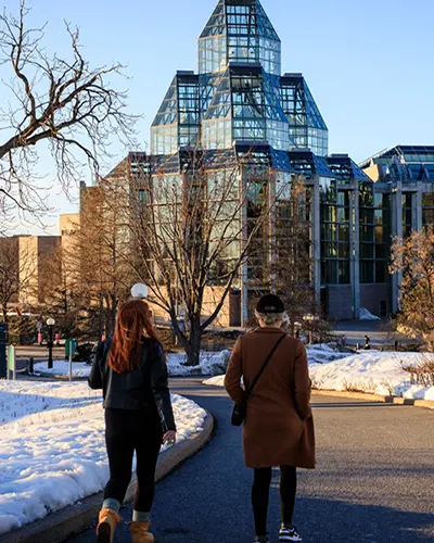 Two women walk towards the National Gallery of Canada in winter.