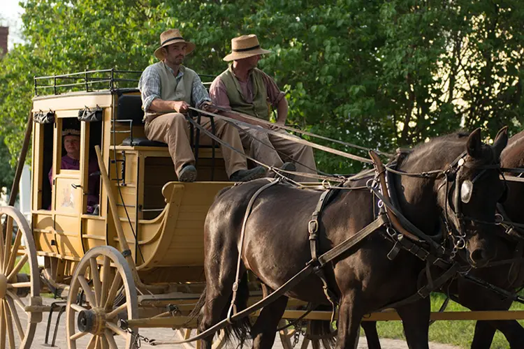 Staff in costume ride a horse and carriage in a recreated 19th-century village.