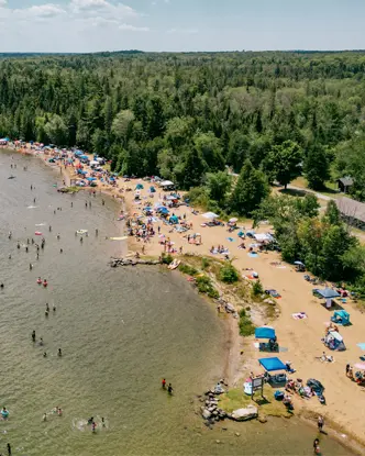 バルサム湖州立公園の賑やかな夏のビーチ。砂浜沿いには遊泳客やパラソルが並んでいます。