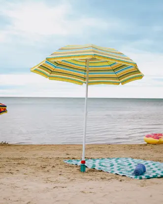 Sombrillas de rayas y una manta estampada colocadas en la orilla arenosa de la playa de Wasaga, con aguas tranquilas y un cielo nocturno melancólico.