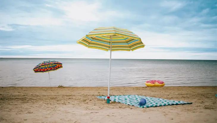  ワサガビーチの砂浜に、穏やかな海と憂鬱な夕空を背景に、ストライプ柄のパラソルと模様のついたブランケットが設置されています。