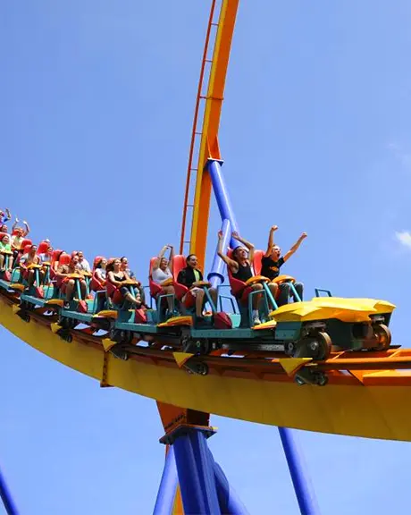 Groupe de personnes, les mains en l’air, à bord d’une montagne russe jaune, orange et bleu à Canada’s Wonderland.