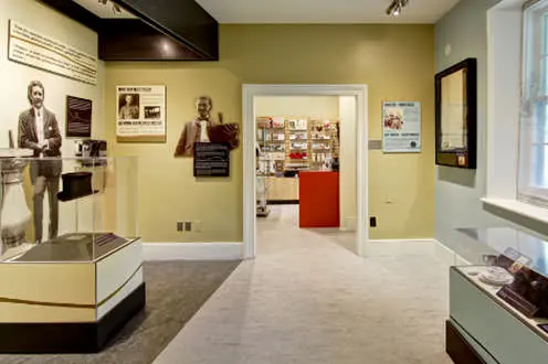 Exposition intérieure à la Maison McCrae, avec présentoirs vitrés, photos et plaques sur les murs.