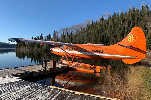Un hidroavión naranja atado al muelle a orillas de un lago.