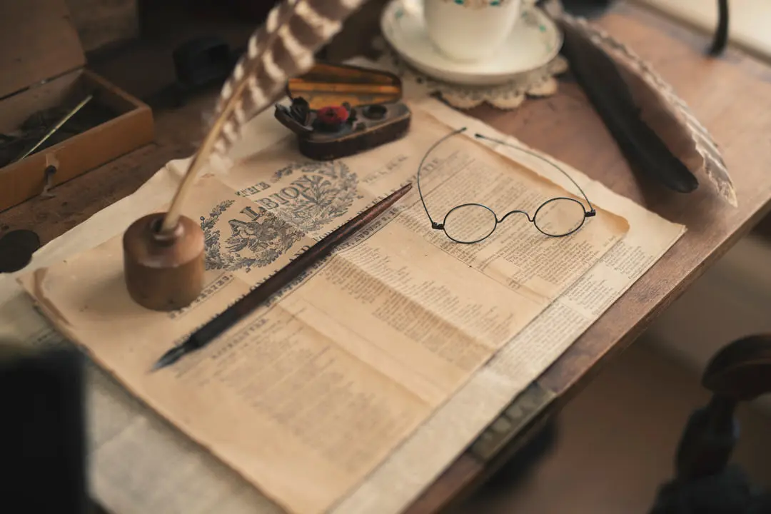 Mesa con taza y platillo de porcelana al lado de la portada del periódico histórico con bolígrafos tradicionales y anteojos de lectura en la parte superior