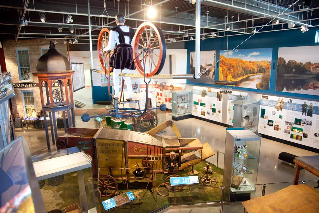 Vue de dos d'un homme se tenant debout entre deux grosses roues de chariot historique et entouré de meubles de pionniers et de photos sur les murs.