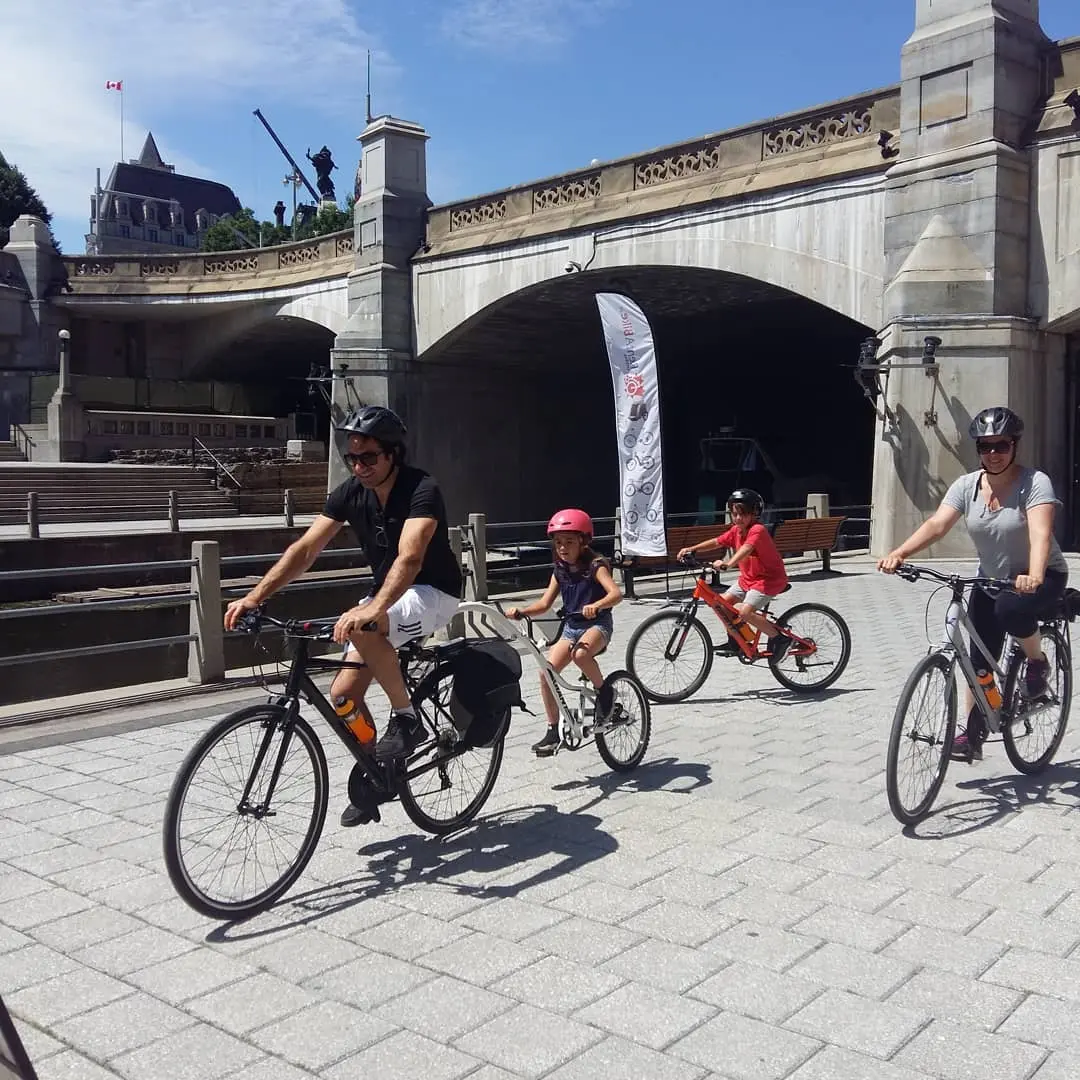 遺産の手すりと高い橋を通過する広い灰色のレンガの小道で自転車に乗る男性と女性と2人の子供