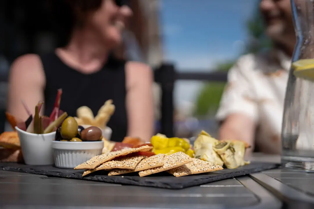 Schwarzes Tablett mit kleinen Schalen aus Rhabarber und Oliven und Crackern und Fingerfood neben einer großen Flasche Wasser mit Zitronenscheiben