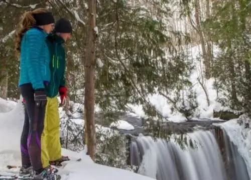 A couple snow shoeing and looking down at the ground