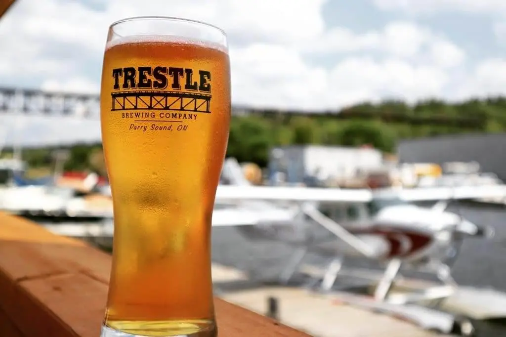 A tall glass of beer resting on a ledge with a floatplane in the background