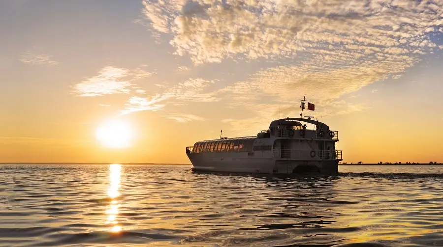 Coucher de soleil derrière un bateau qui navigue sur l’eau. 
