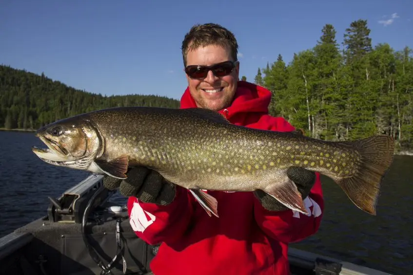 Un homme souriant dans un bateau sur un lac, tient un gros poisson