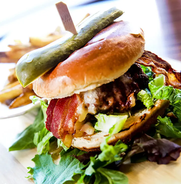 きゅうりのピクルスをトッピングした野菜とベーコンを重ねたハンバーガー