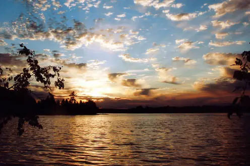 The sun hangs low behind the clouds and over the lake creating an orange glow in the reflection on the water. 