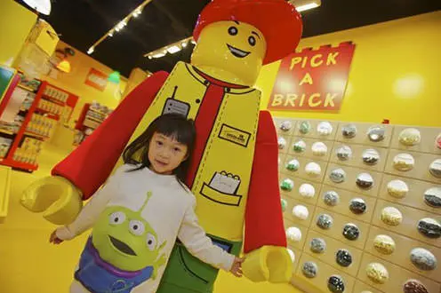 Niño parado frente a una gran estatua de persona Lego.