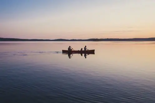 A couple and their dog in a canoe paddle across a quiet lake