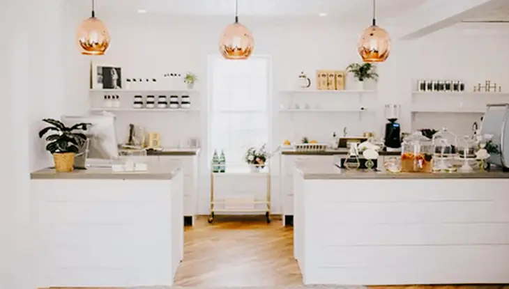  Interior moderno y luminoso de Bloomfield Beauty Co., con gabinetes blancos, luces colgantes ruborizadas y un mostrador de venta minorista de spa limpio.