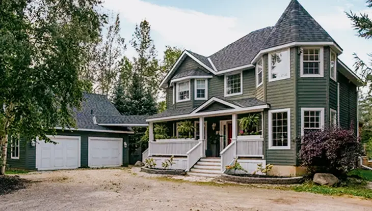 Craigleith Manor Boutique Bed and Breakfast, a green cottage with white trim, front porch, and detached garage, surrounded by tall trees.