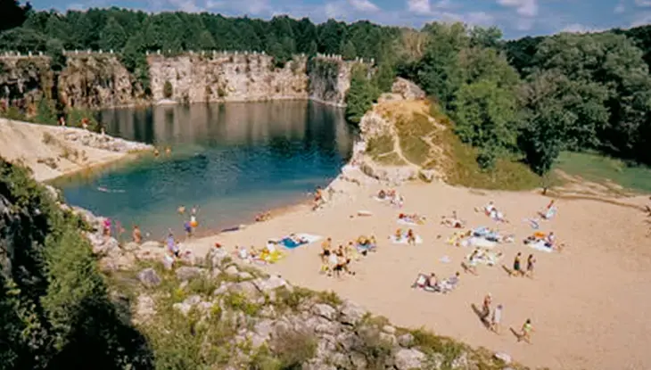 Playa de arena con visitantes relajándose y nadando, rodeada de acantilados en el Área de Conservación de Elora Quarry.