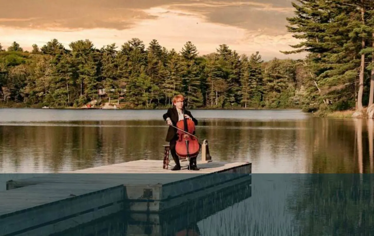 Un homme jouant du violoncelle sur un petit quai flottant entouré de forêt à Parry Sound.