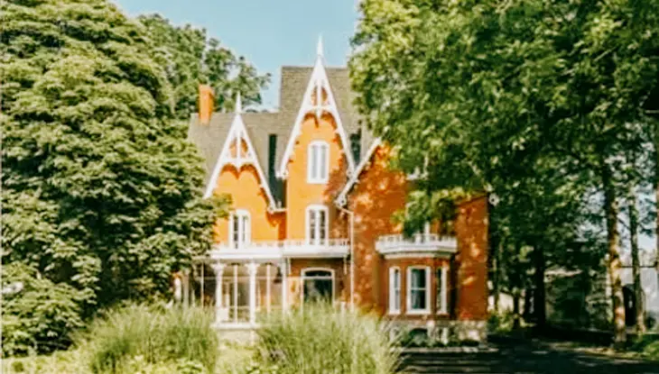  Una casa de estilo neogótico de ladrillo rojo con molduras blancas, frontones puntiagudos y un exuberante entorno verde llamada Merrill House en el condado de Prince Edward.