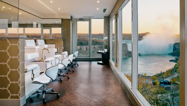 Luxueux salon de spa avec postes de manucure devant des fenêtres allant du sol au plafond et donnant sur les chutes Niagara.