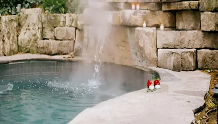 ナイアガラ・オン・ザ・レイクの 100 ファウンテン スパでは、石壁と、凹凸のある石壁の上に置かれたキャンドルのある静かなスパ プールから湯気が立ち上っています。