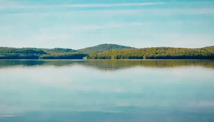Still blue waters reflecting tree-covered hills under a clear sky at Windy Lake Provincial Park in Ontario.