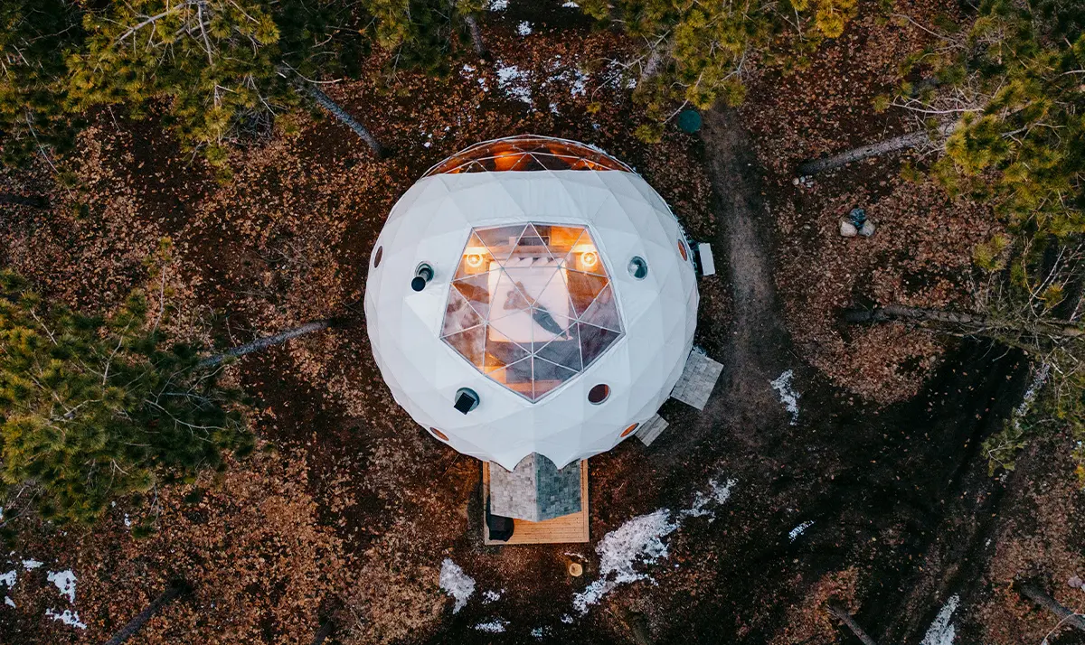 Geodesic dome nestled among trees in Glen Oro, glowing warmly in a serene, snow-dusted forest.