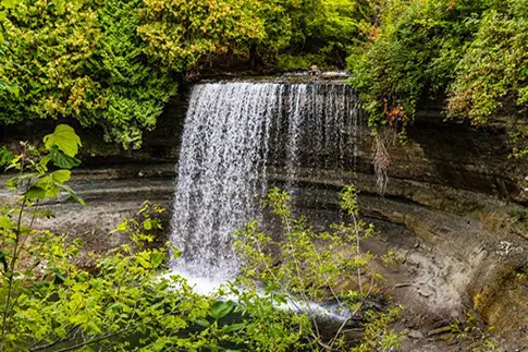 Von Grün umgebener Wasserfall, der in ein Becken am Fuße des Wasserfalls stürzt.