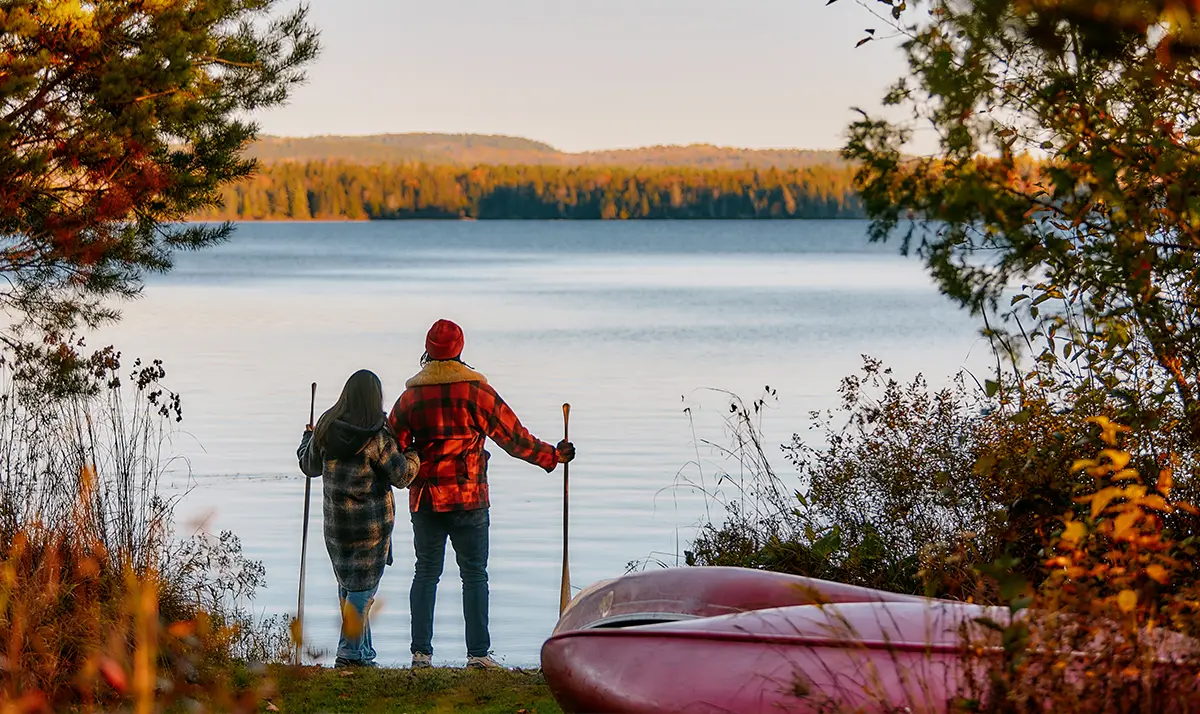 Deux personnes faisant de la randonnée avec des bâtons et regardant l’eau sereine et les arbres d’automne au Killarney Lodge, dans le parc Algonquin.