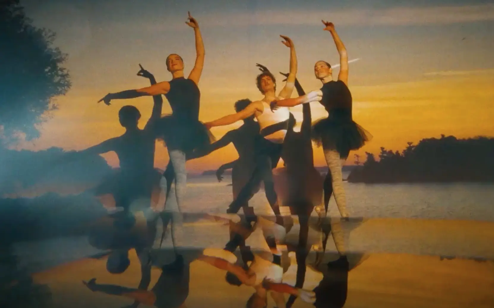 Danseurs de ballet se produisant devant une toile de coucher de soleil, avec de gracieux reflets sur un plancher de scène brillant.