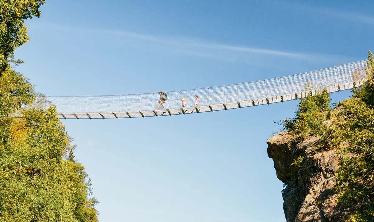 Three people walking across White River Suspension Bridge in Pukaskwa National Park, Heron Bay, Ontario.