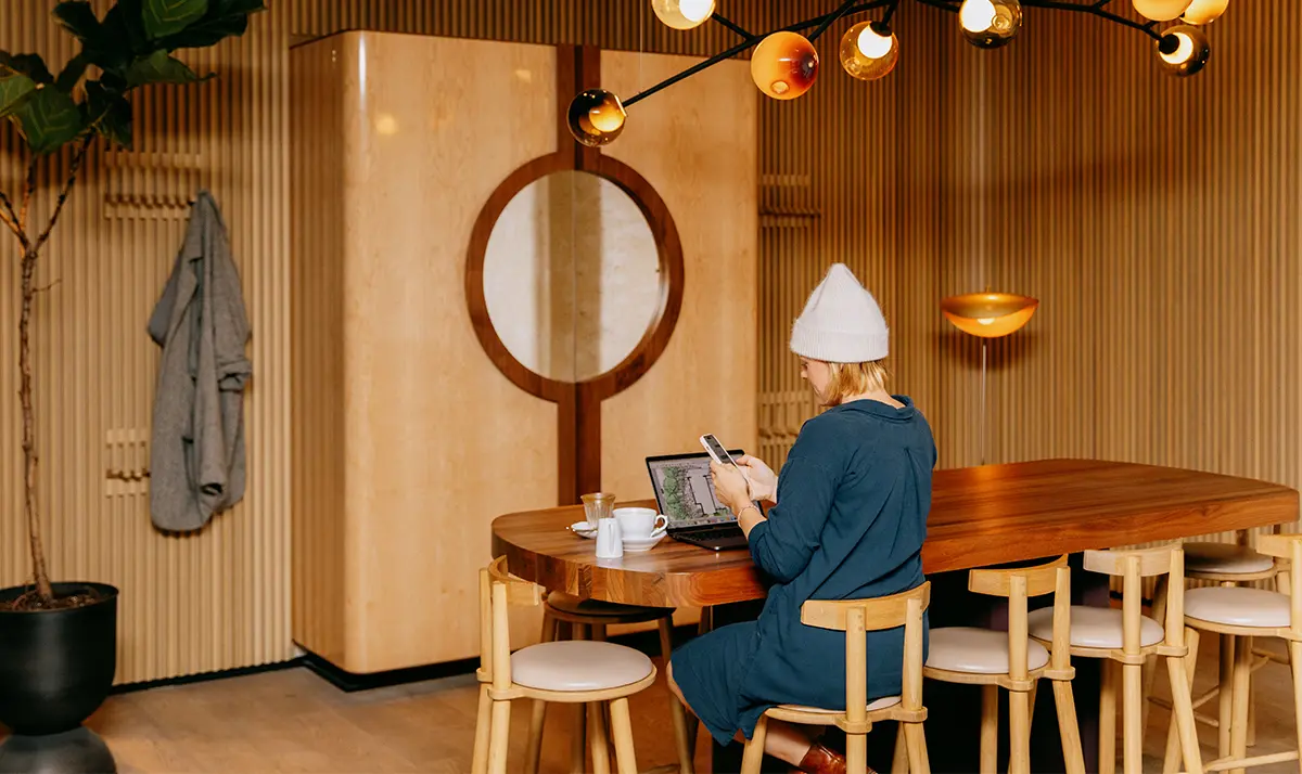 Personne assise à une table en bois devant un ordinateur portable et un téléphone intelligent dans une pièce moderne de l’hôtel Royal à Picton.