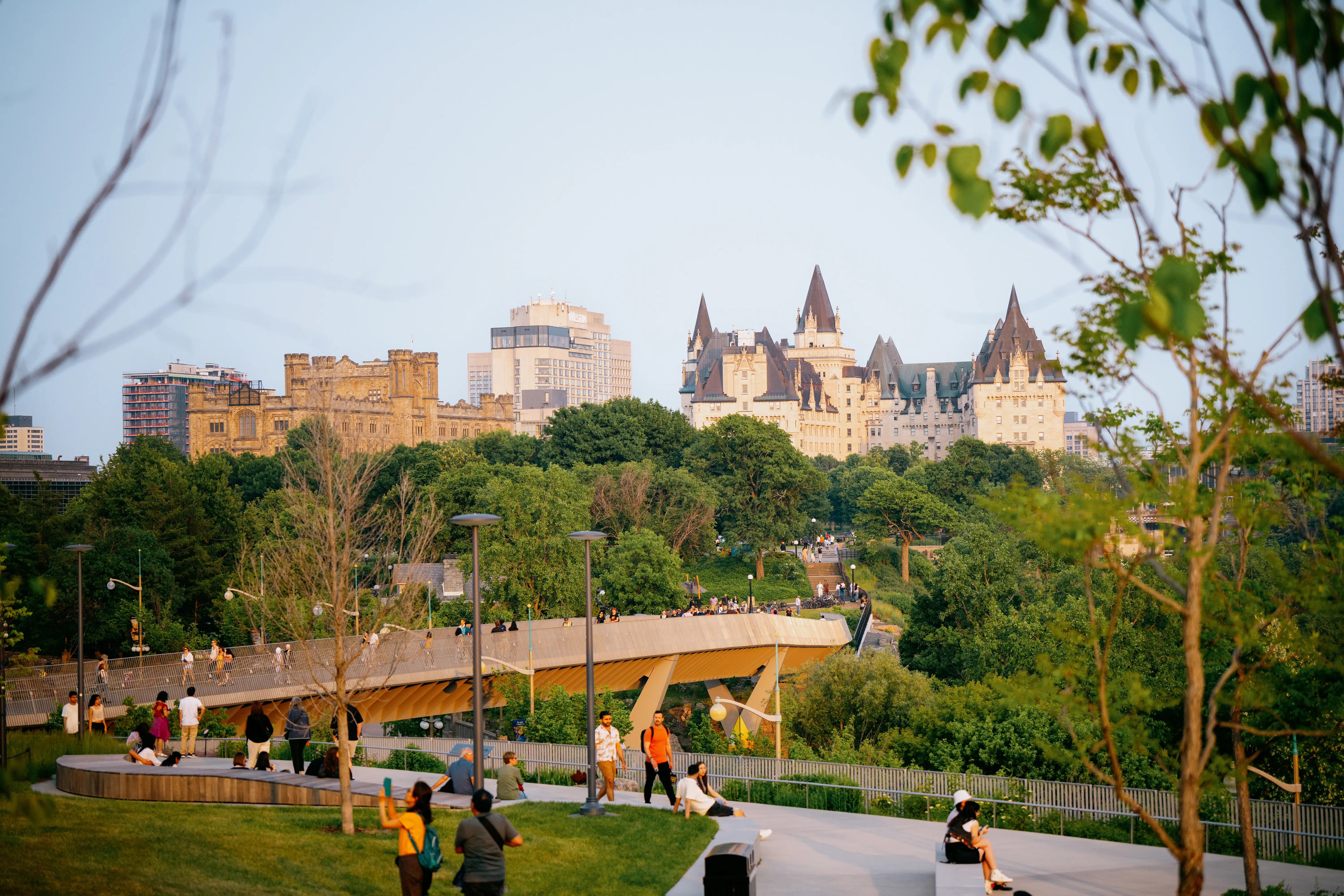La pointe Kìwekì à Ottawa, remplie de gens et d’arbres verts avec, au loin, l’élégant Fairmont Château Laurier.