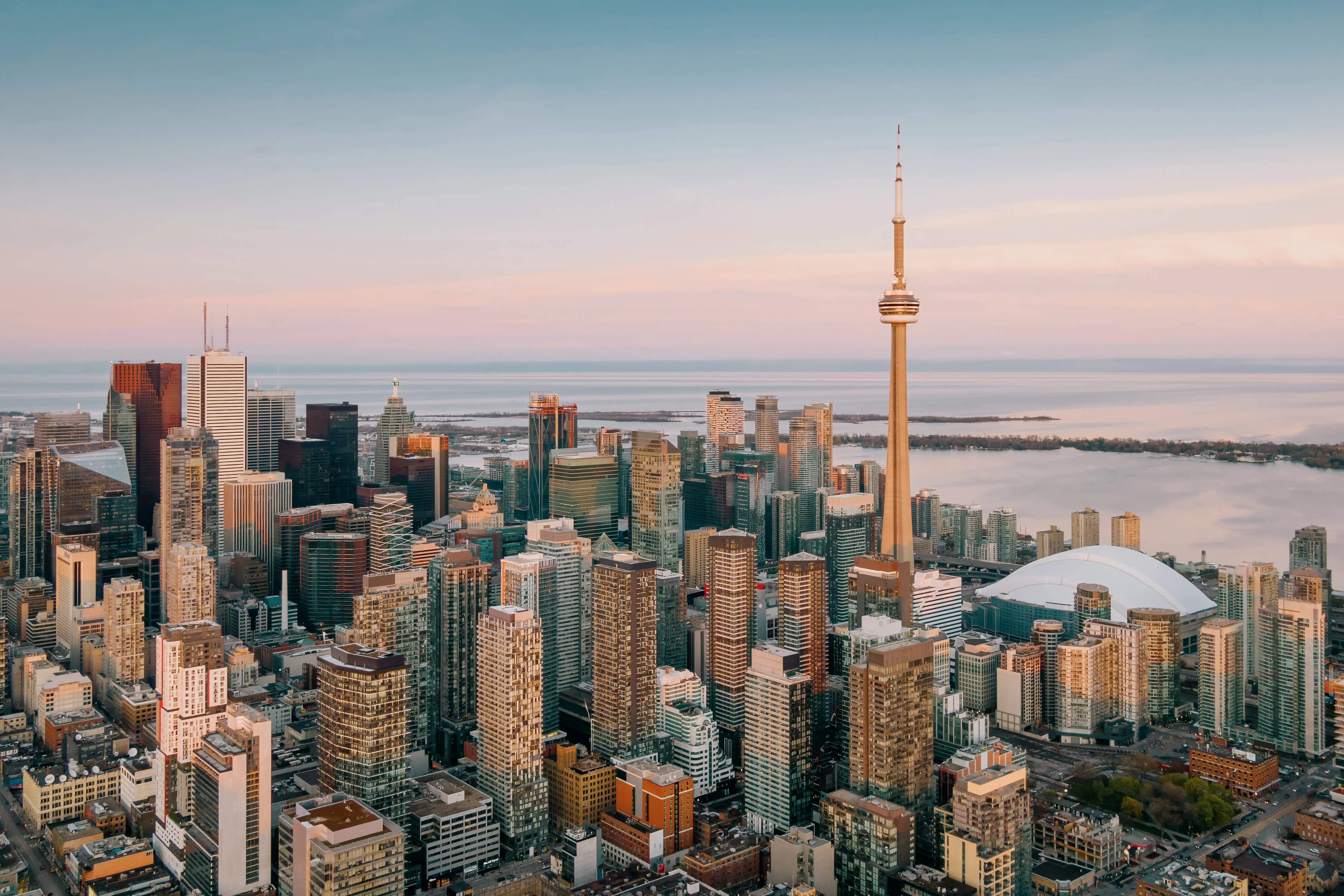 A birds-eye-view of downtown Toronto, glowing under a pink sunset, with the CN Tower in view.