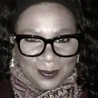 Portrait de Debra Mansillo, souriant délicatement et portant une veste et une écharpe foncées.