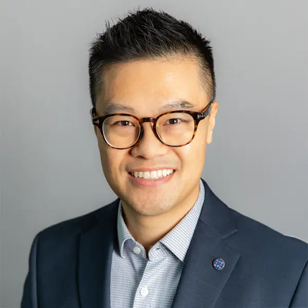 Portrait de Ronald Ting, souriant et portant une chemise et un blazer foncé.
