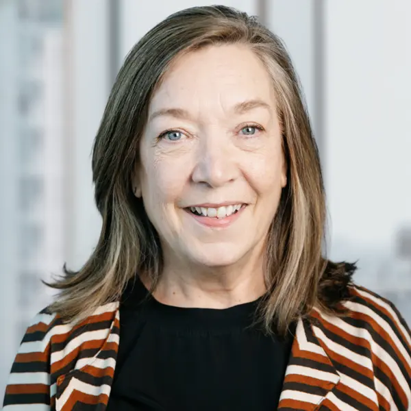 Portrait de Cathy Kirkpatrick, souriant et portant un chemisier noir et une veste à rayures.