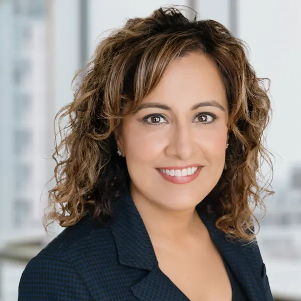 Portrait de Jasveen Rattan, Ph. D., souriant et portant un chemisier et un blazer noirs.