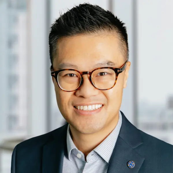 Portrait de Ronald Ting, souriant et portant une chemise et un blazer foncé.