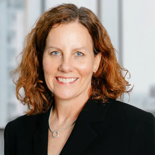 Portrait de Sue Harrison, souriant et portant un blazer noir.