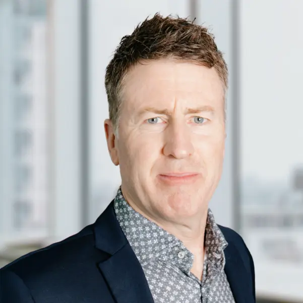 Portrait de Todd Eastman, souriant et portant une veste de costume foncée et une chemise.