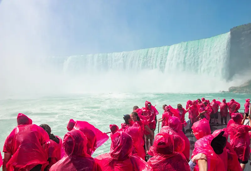 赤いレインポンチョを着た人々が滝に近づきながら船のデッキに立っています。