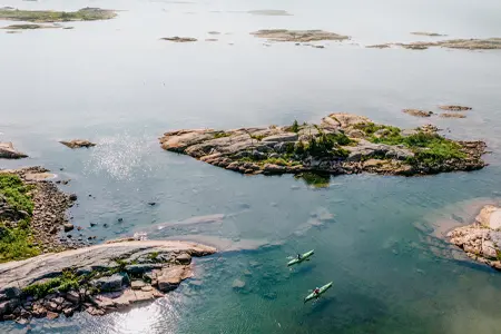 Two kayakers paddling through clear water among rocky islands in Georgian Bay.