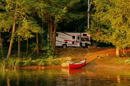 RV parked at a forested lakeside campsite in Haliburton Forest with a red canoe on the shore.