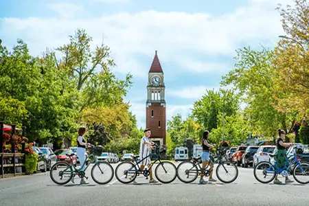 Four cyclists walking their bicycles across the street in Niagara-on-the-lake in front of the clock tower.