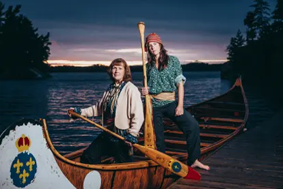 Two people canoeing on a lake at sunset, with one holding a paddle and the other standing in the canoe.