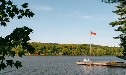 Vue sur un lac à Muskoka, en Ontario, avec un drapeau canadien flottant au-dessus d’un quai.