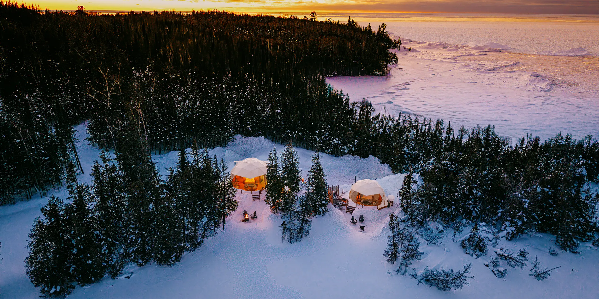 Aerial view of a snowy lakeside landscape in Ontario, with two cabins surrounded by trees.